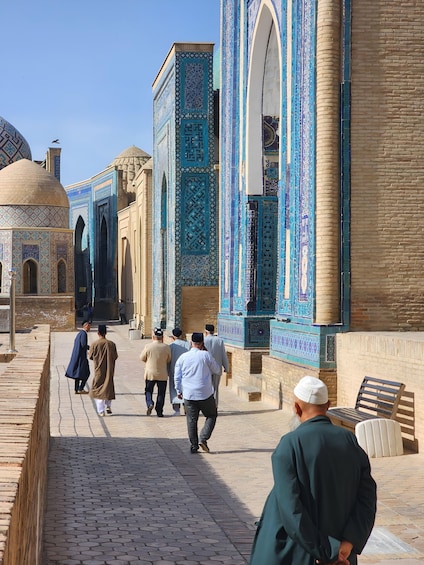 A group of people walking along a street lined with buildings featuring intricate blue tile work. 5