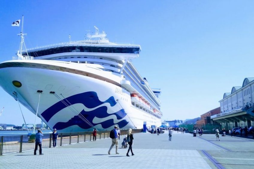 Un gran crucero atracado en un puerto, con gente caminando por el paseo marítimo. 4
