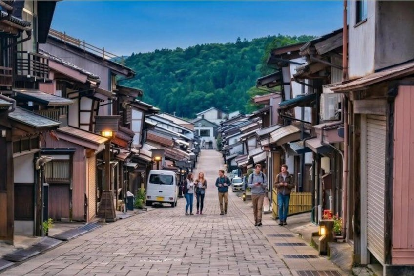 A cobblestone street lined with traditional buildings, a van, and people walking. 3