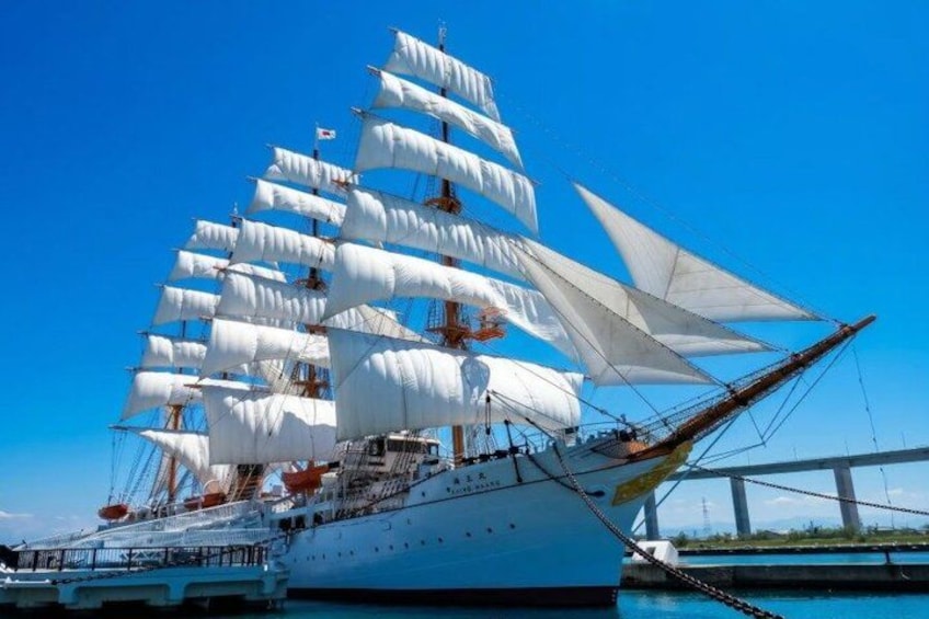 A large sailing ship with multiple masts and white sails docked at a pier. 1