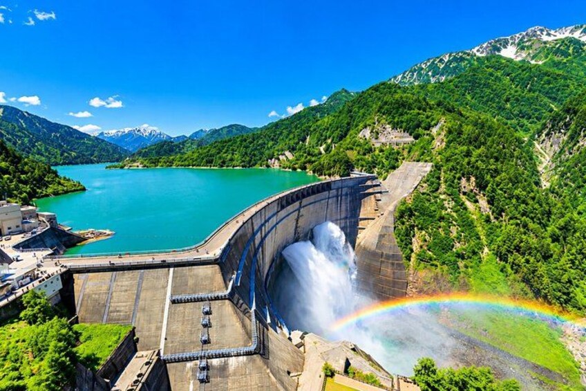 Een dam met een waterval, een regenboog en een meer omringd door bergen. 4