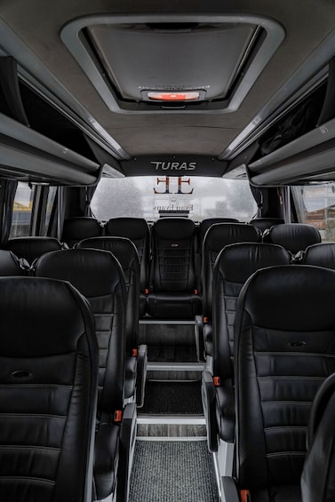 The interior of a bus with black leather seats, a central aisle, and a sign reading 'TURAS' on the back wall. 2