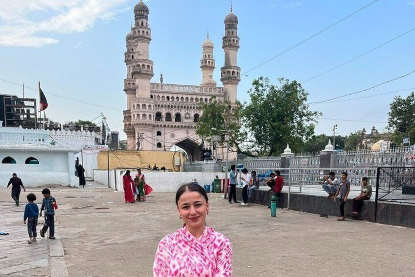 Eine Moschee mit zwei Minaretten, eine Gruppe von Menschen, die auf einer Mauer sitzen, und einige Personen, die entlanggehen. 3