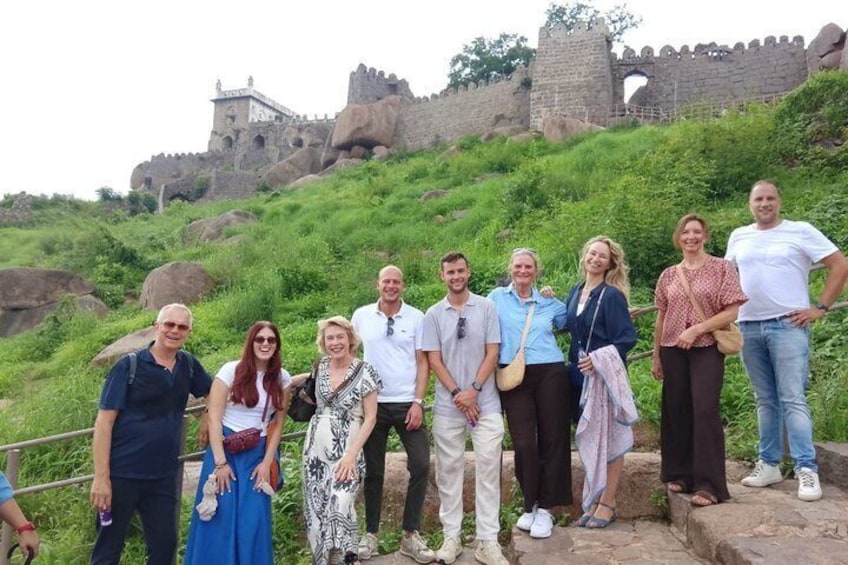 Eine Gruppe von Personen steht auf einer Steinterrasse, im Hintergrund eine historische Steinmauer und ein Schloss. 1