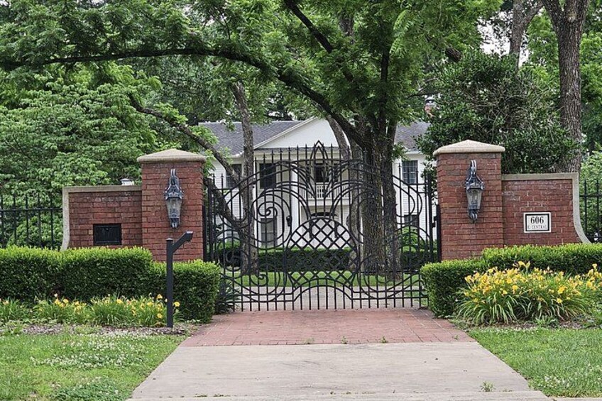 A gated entrance with a brick wall, a metal gate, and a house in the background. 5