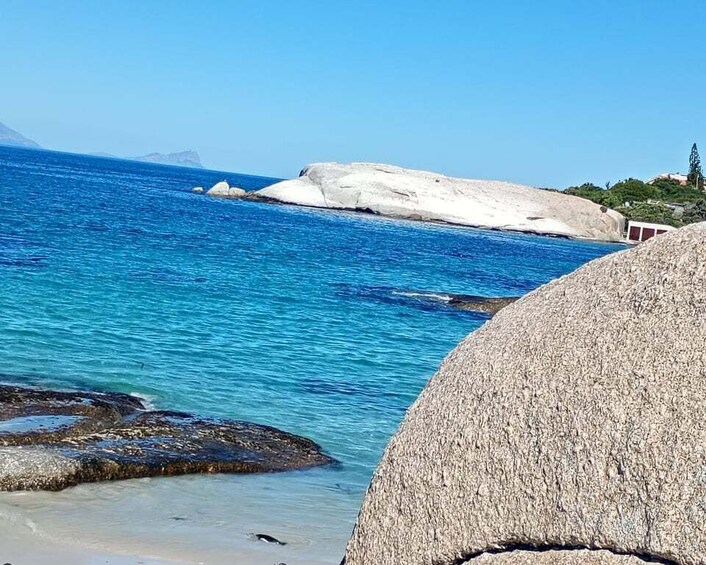 A coastal landscape with clear blue water, large rocks, and distant mountains. 2