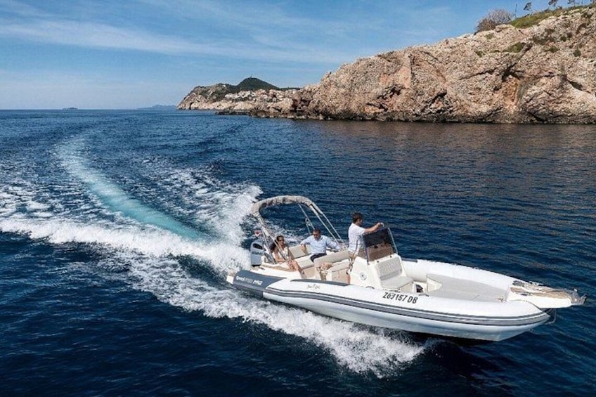A speedboat with two people on board, moving through a body of water with a rocky coastline in the background. 2