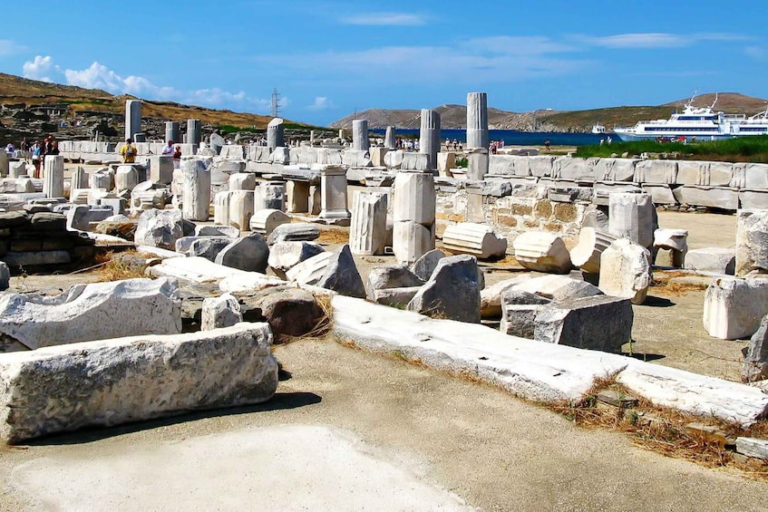 Ancient ruins with columns and stone blocks, a clear sky, and a cruise ship in the background. 3