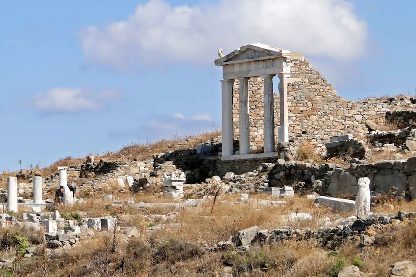 Ancient ruins with columns and a stone structure on a hillside. 1