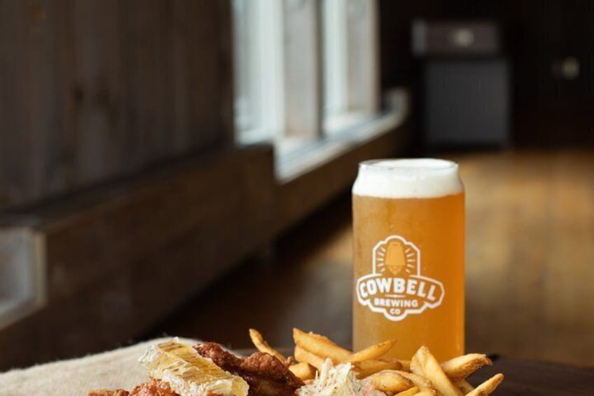 A glass of beer with a label reading 'Cowbell Brewing Co.' next to a plate of food. 3