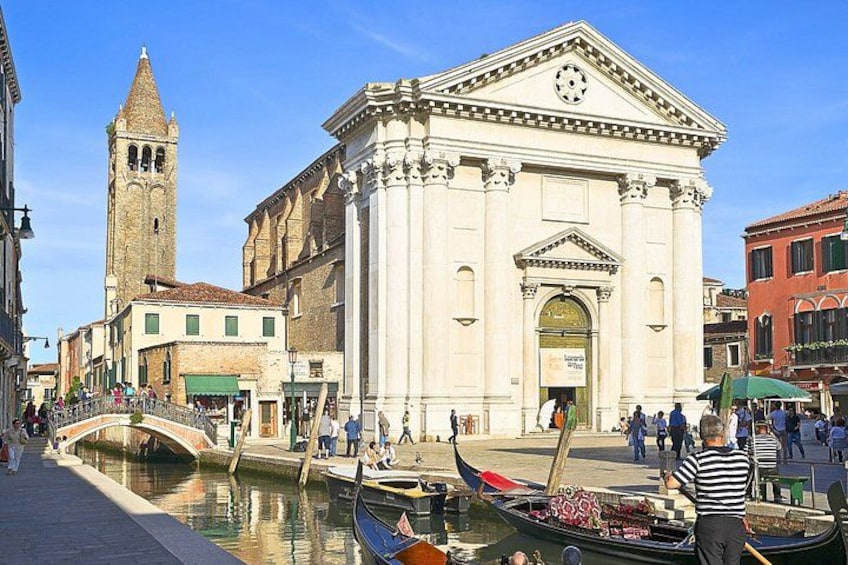 A canal with gondolas, a historic building with a clock tower, and people walking. 2