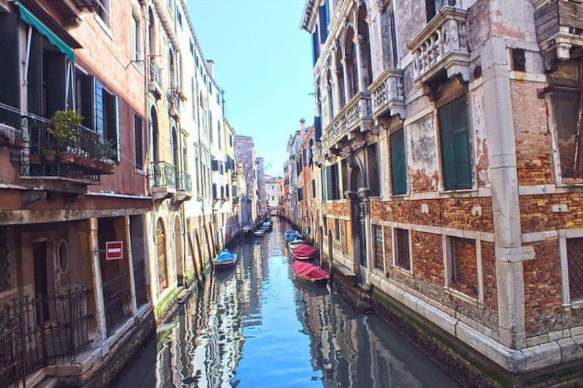 A narrow canal flanked by historic buildings with balconies and a row of boats. 5