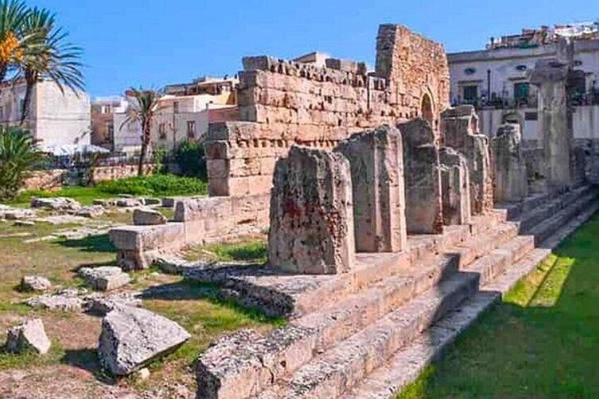 Ancient ruins with stone columns and steps, surrounded by modern buildings and greenery. 5