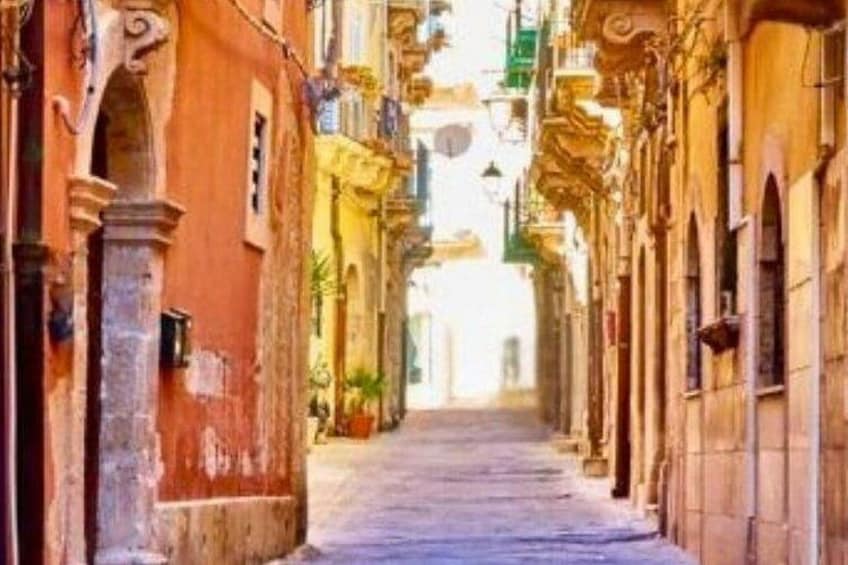 A narrow street with buildings on either side, some with balconies and decorative elements. 4