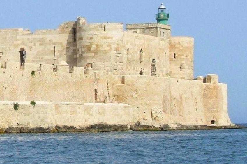 A large stone fortress with a lighthouse on top, situated by the sea. 1