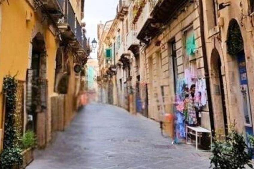 A narrow street with buildings on either side, some with balconies and others with windows. 2