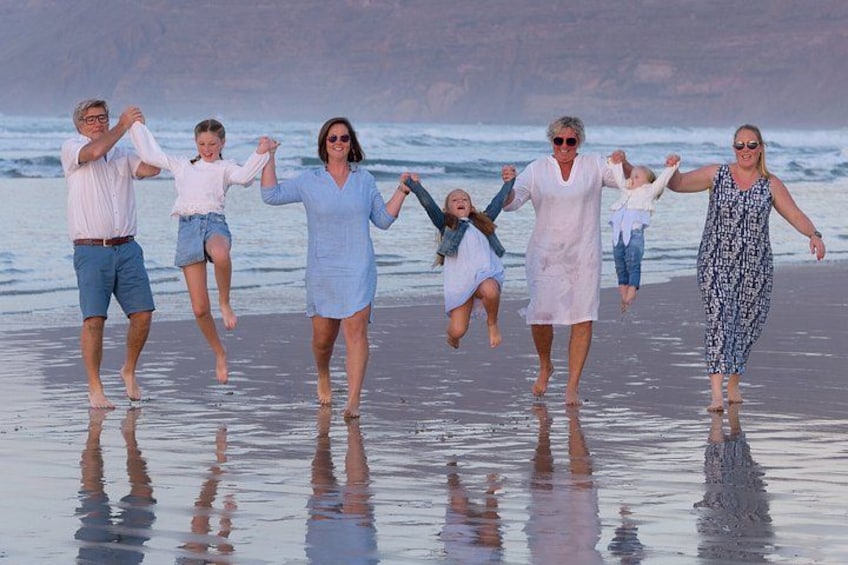 En familie på seks går en tur på stranden med bølger i baggrunden. 5
