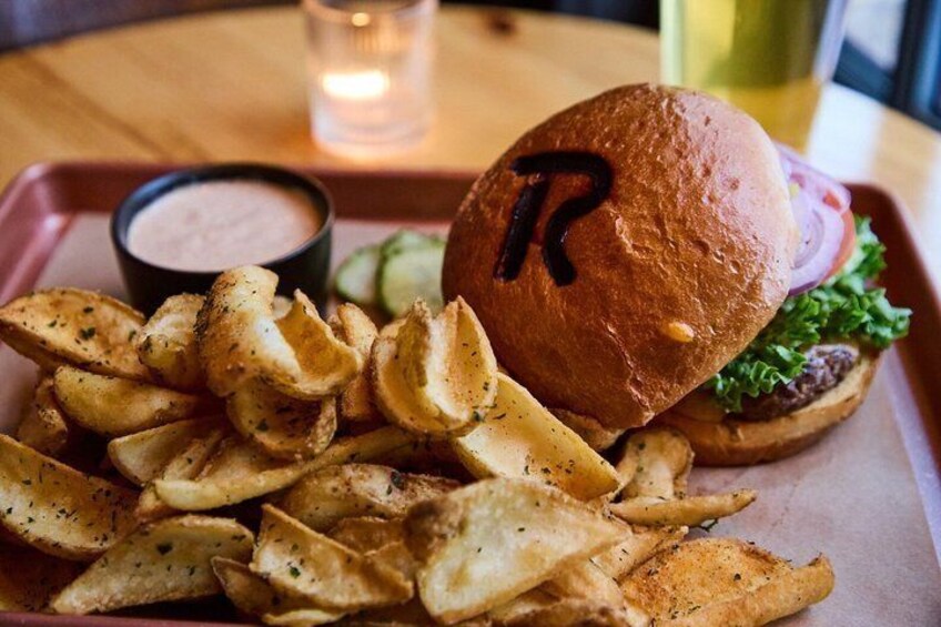 A burger with a letter 'R' on the bun, a side of seasoned fries, and a small bowl of sauce. 5