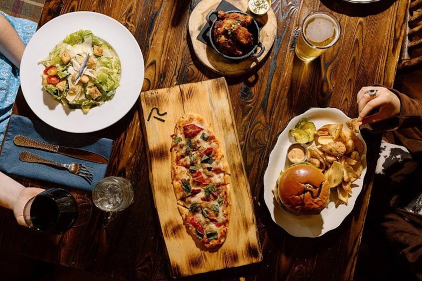 Una mesa de madera con varios alimentos, incluyendo pizza, ensalada, hamburguesa y papas fritas. 5