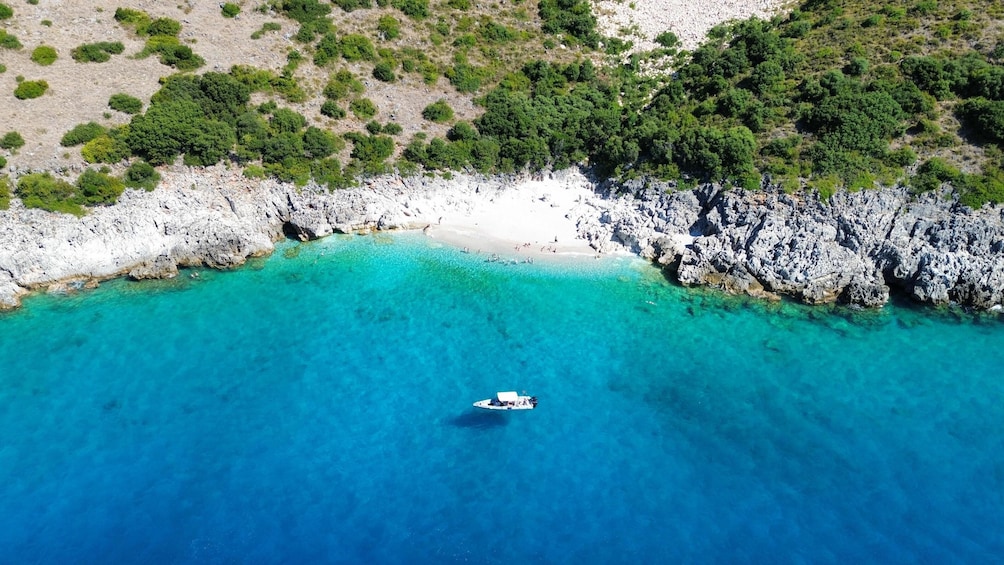 An aerial view of a coastal area with clear turquoise waters, a rocky shoreline, and a boat in the water. 3