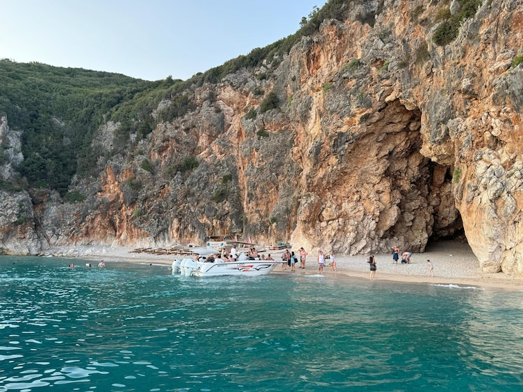 A rocky coastline with a boat docked at the beach and people near the water. 1