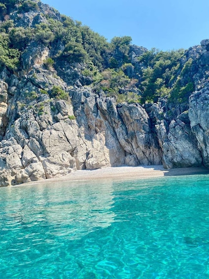 A coastal landscape with clear turquoise water, rocky cliffs, and a sandy beach. 5