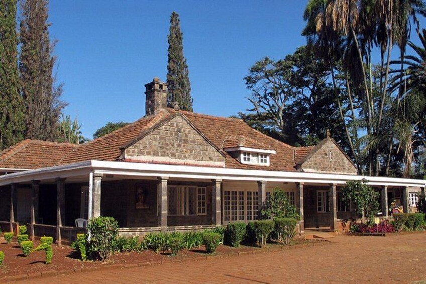 A stone house with a tiled roof, surrounded by greenery and tall trees. 2