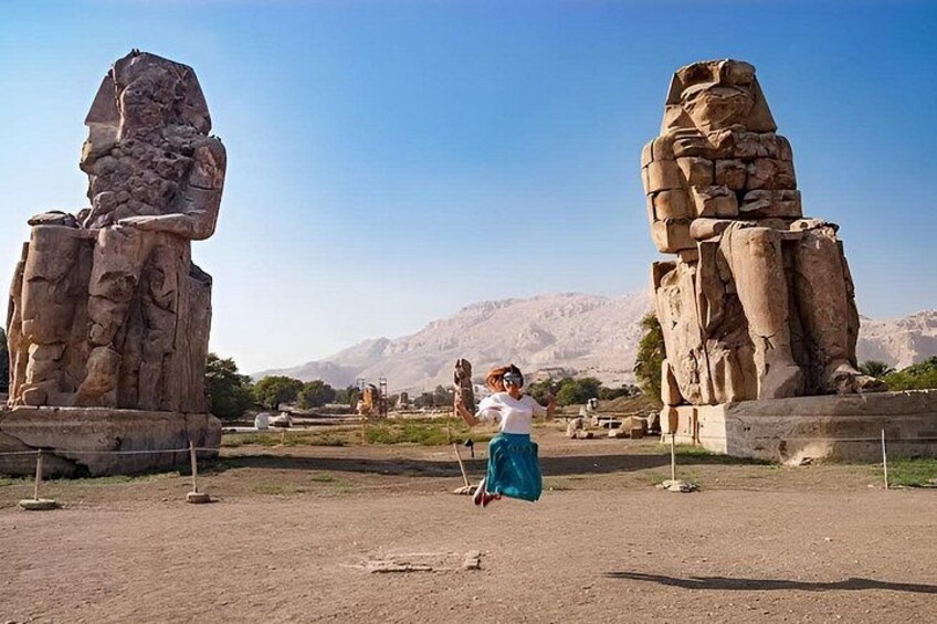 A person standing between two large stone statues in a desert landscape with mountains in the background. 4