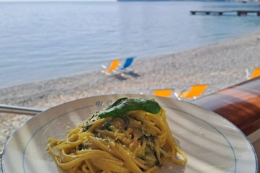 Spaghetti med grøn pynt, en strand med liggestole, og et vandareal i baggrunden. 5
