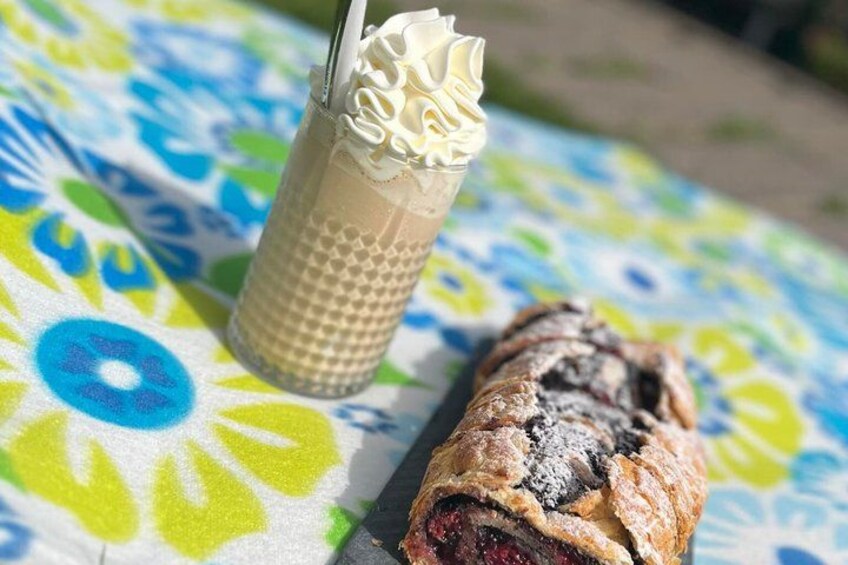 A beverage in a glass with whipped cream, a pastry on a tablecloth with a floral pattern. 2