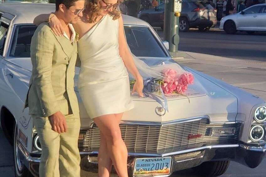 Une voiture ancienne avec une plaque d’immatriculation du Nevada, un homme en costume vert clair et une femme en robe blanche, tous les trois debout à côté de la voiture. 3