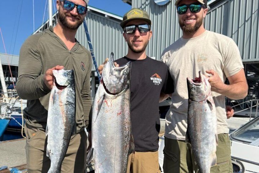 Three individuals holding fish, a boat, and a building in the background. 5