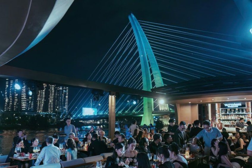 A crowded outdoor dining area with a modern bridge in the background. 2