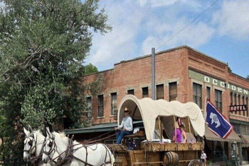 Een overdekte wagen met paarden voor een bakstenen gebouw waarop 'Occidental Hotel' staat. 1
