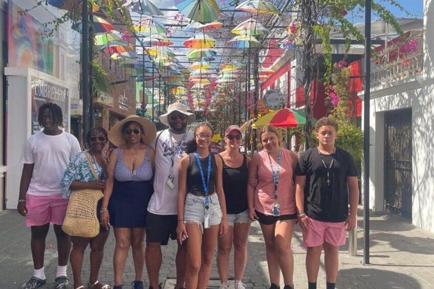 A group of people standing on a sidewalk under colorful umbrellas. 5
