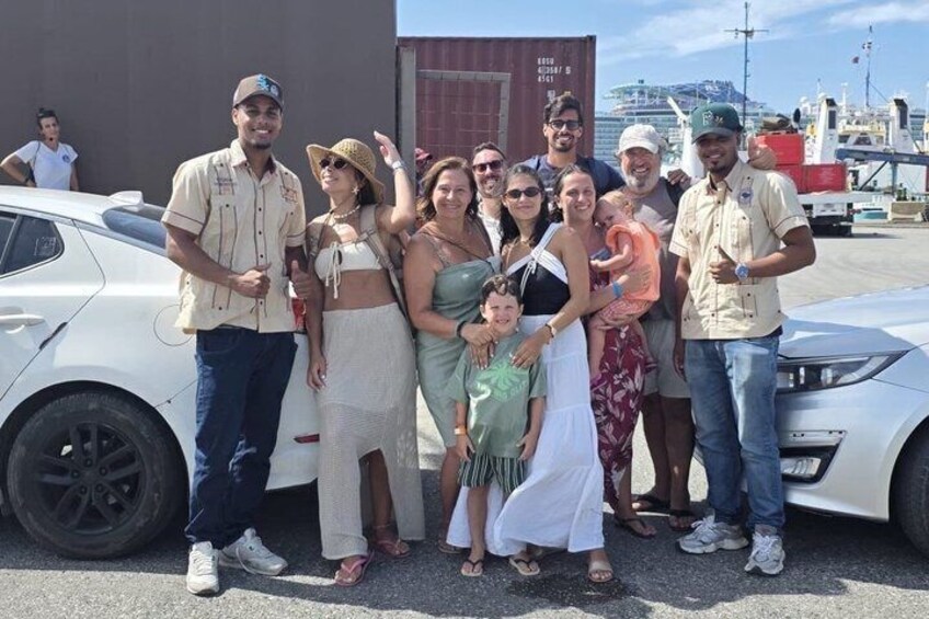 A group of people posing in front of a white car and a shipping container. 4