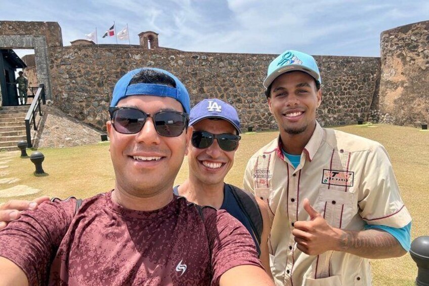 Three people in front of a stone wall with a staircase leading up to a building. 3
