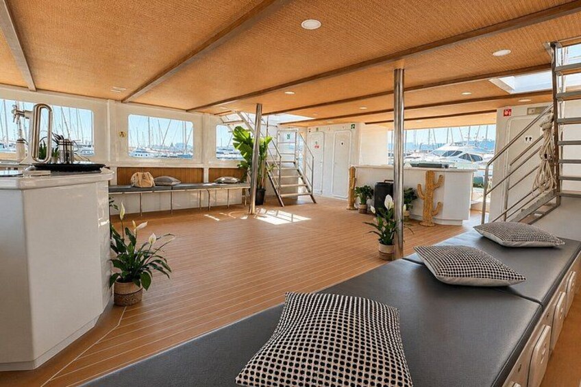 A yacht interior with a wooden deck, a dining area, and a view of the marina. 5