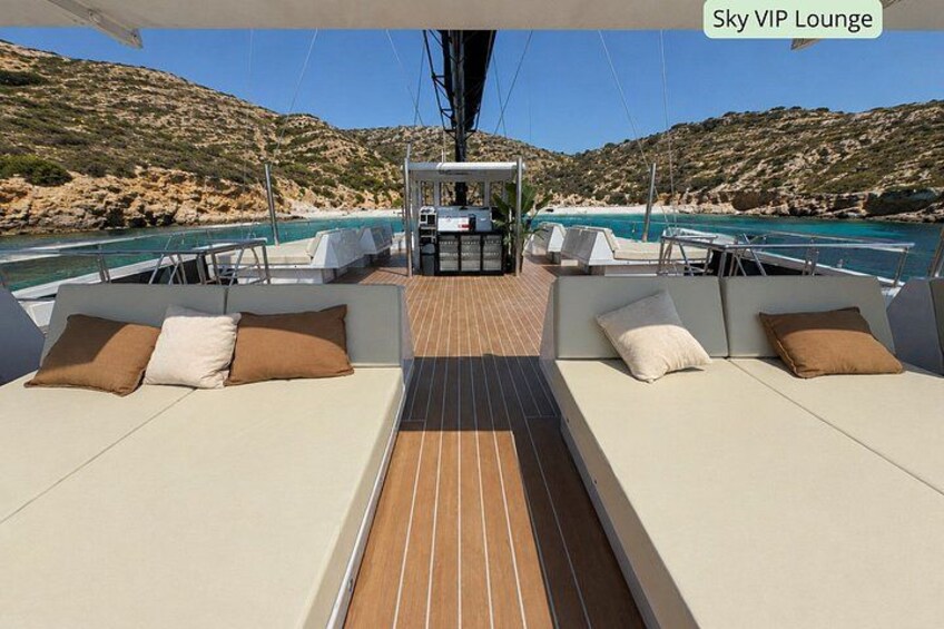 A yacht's Sky VIP Lounge with a wooden deck, cushioned seating, and a view of the coastline. 4