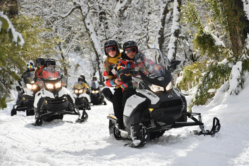 A group of snowmobiles on a snowy trail with trees on the sides. 1