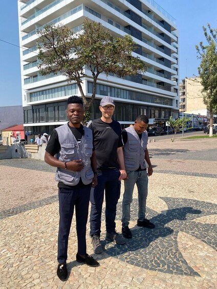 Three men standing on a cobblestone street with a modern building in the background. 4