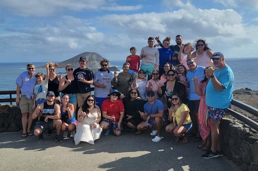 A group of people posing on a coastal road with a mountain in the background. 2