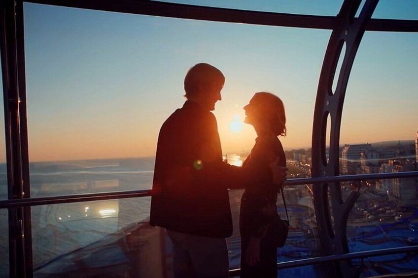 Un couple s’embrasse sur un balcon donnant sur une vue panoramique de la ville au coucher du soleil. 1