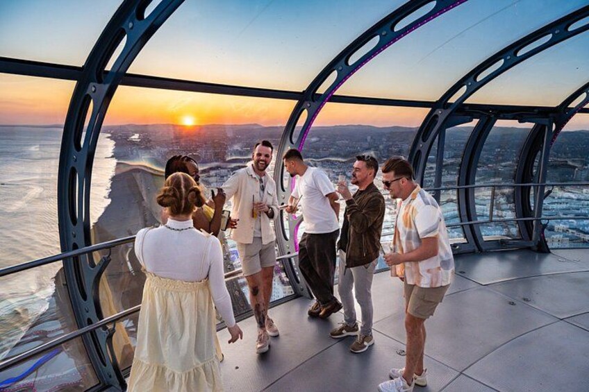 Un groupe de personnes se tient sur un plancher de verre, avec une vue sur la ville et un coucher de soleil en arrière-plan. 5