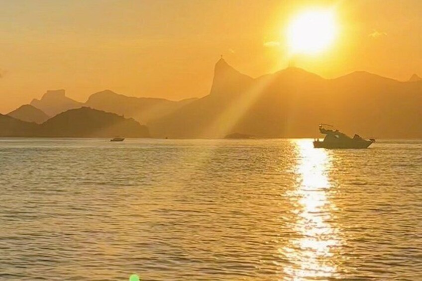 A sunset over a calm sea with a boat and distant mountains. 2