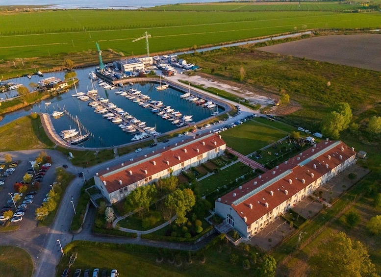 A marina with boats docked, a large building complex, and surrounding green fields. 5