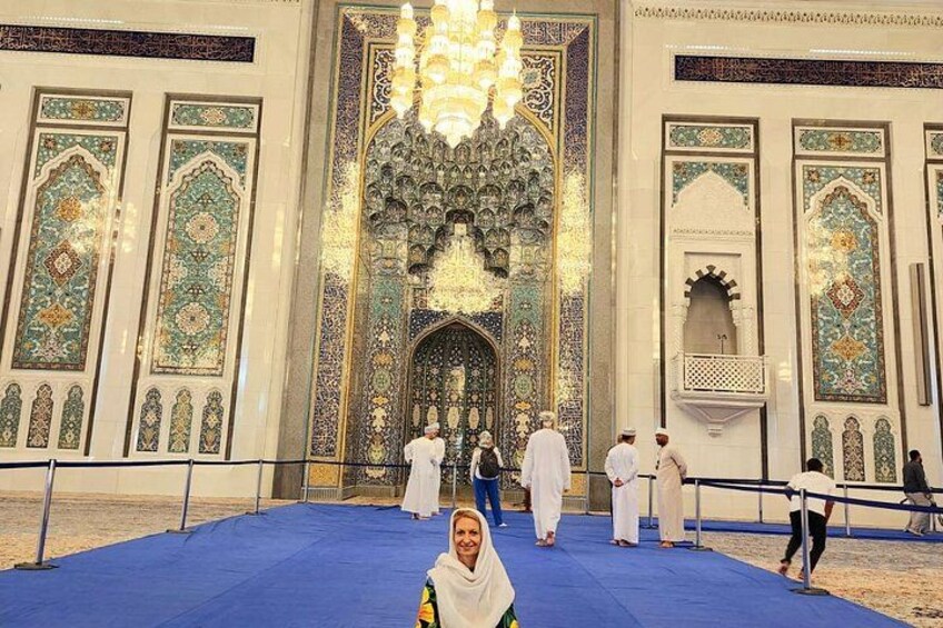 A mosque interior with intricate tile work and a large chandelier. 1