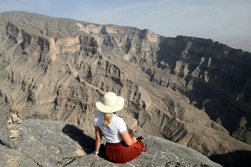 A person sitting on a rocky outcrop overlooking a canyon with layered rock formations. 2