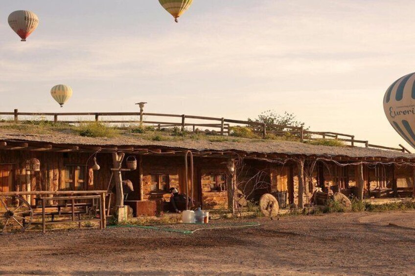 Una construcción rústica de madera con techo de paja, rodeada de terreno de tierra y una cerca de madera. 3