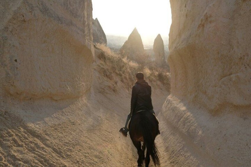 Una persona montando a caballo por un cañón estrecho con imponentes formaciones rocosas. 1
